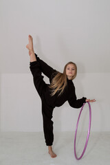 A young rhythmic gymnast in a black tracksuit performs elements with a hoop