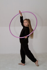 A young rhythmic gymnast in a black tracksuit performs elements with a hoop