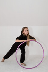 A young rhythmic gymnast in a black tracksuit performs elements with a hoop