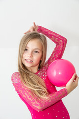 A young rhythmic gymnast in a bright pink leotard is training with a ball