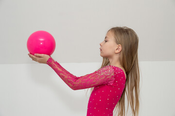 A young rhythmic gymnast in a bright pink leotard is training with a ball