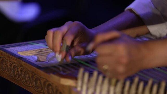 Close-up of musician's hands playing the Qanun. The artist plucks strings and adjusts tuning levers on this traditional Middle Eastern string instrument during a live musical concert performance.

