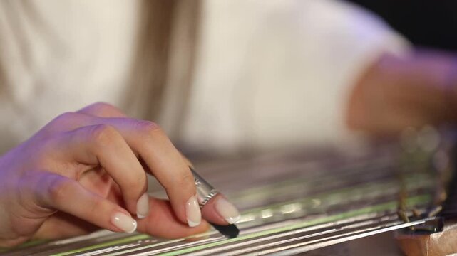 Close-up of musician's hands playing the Qanun. The artist plucks strings and adjusts tuning levers on this traditional Middle Eastern string instrument during a live musical concert performance.

