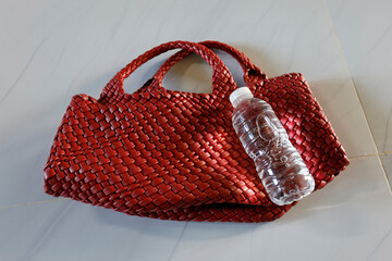 Portable clear water bottle on a red leather bag, reflecting a health-conscious lifestyle and...