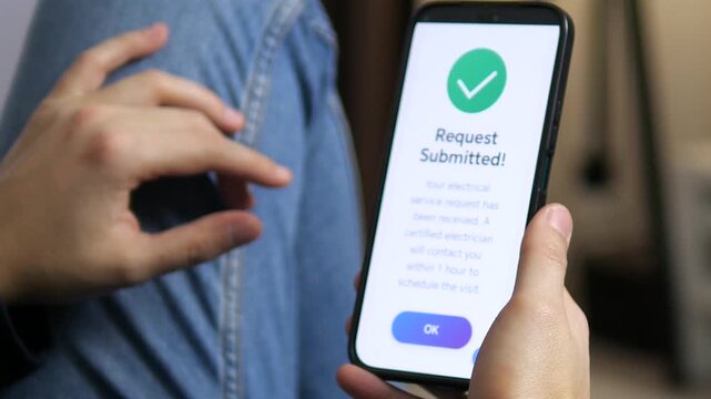 his slow motion video shows a man's hands holding a phone with an app for booking home services. He carefully reads the details before ordering an electrician with a single tap, followed by a