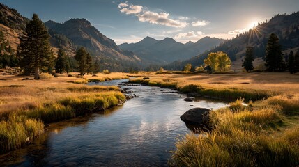 Fototapeta premium Winding river cutting through a golden autumn meadow with a sunburst rising over distant mountains in a serene valley landscape.