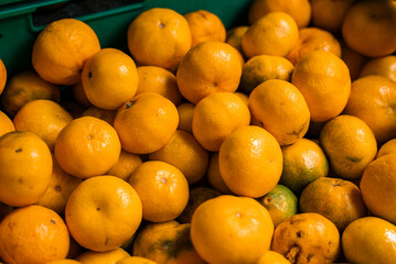 A close view shows glossy tangerines piled in a green crate at a market in Funchal, Madeira, with orange and green skins and warm light highlighting dimpled texture.