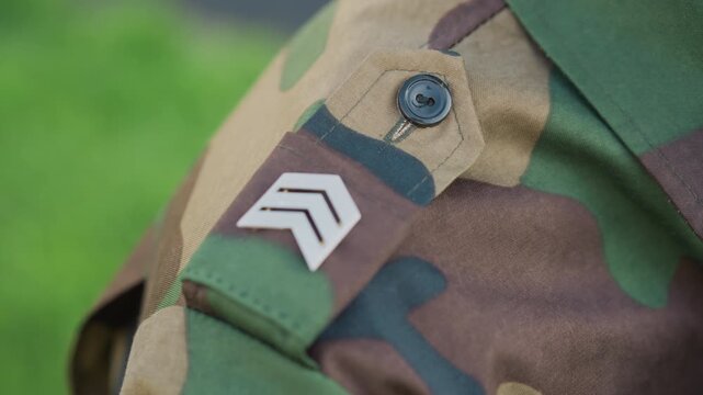Veteran Confidently Displays Insignia Outdoors, An Experienced Military Veteran Carefully Aligns His Rank Patch With Expression Of Dignity And Remembrance In Serene Outdoor Environment