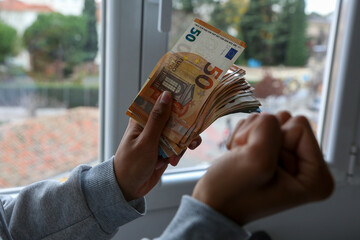 A wad of euro banknotes held by the hands of a light-skinned African American woman celebrating that she has that money