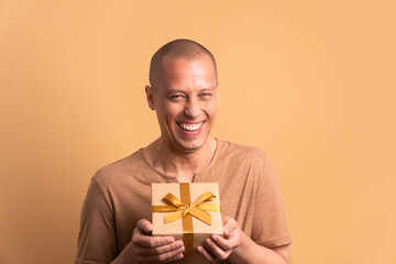 fun bald man receiving gift box in beige studio background. christmas, happy birthday, celebration...
