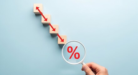 Hand holding magnifying glass over percentage symbol near descending wooden blocks showing rate decrease