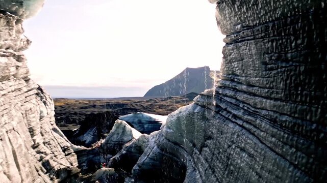 Cinematic aerial drone flight through Katla ice cave tunnel showing blue ice with black volcanic ash veins and green mossy mountains in Iceland 4K.