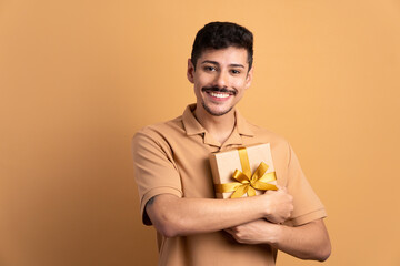 cheerful brazilian man receiving gift box in all beige colors. birthday, christmas, gift box concept.