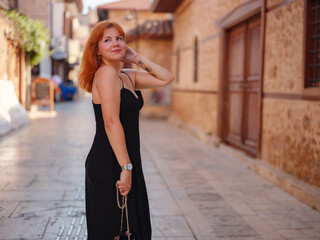 Young woman in elegant black dress walking in cozy old town Keleci, Antalya, Turkey during summer day. female traveler discover interesting places and popular attractions