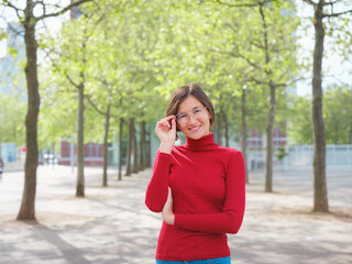 Woman in glasses and red turtleneck, dressed in business style, stands in center of Frankfurt, surrounded by modern buildings and urban life, embodying professionalism and confidence