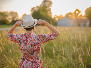 Young woman walking through picturesque European field in late summer. Golden sunlight, lush greenery, and serene rural atmosphere create peaceful countryside scene.