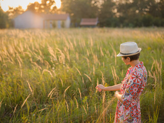 Young woman walking through picturesque European field in late summer. Golden sunlight, lush greenery, and serene rural atmosphere create peaceful countryside scene.
