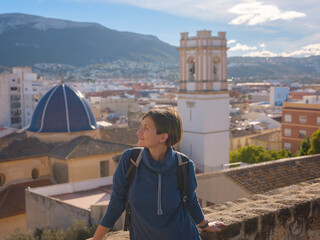 Young woman exploring historic castle in Denia, Alicante province, Spain, scenic views of town below, set against cooler season backdrop. blend of history and tranquility in timeless setting.