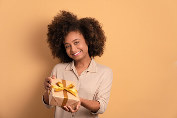 joyful afro brazilian woman with gift box present in beige colors. birthday, christmas, gift box concept.