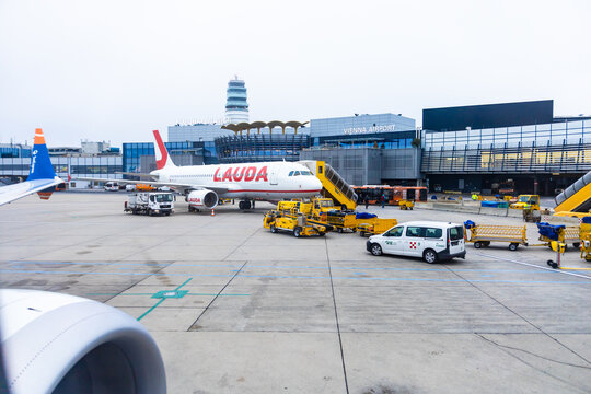 Vienna, Austria - 15 December, 2025: Vienna International Airport scene with a Lauda airplane on the tarmac. Ground vehicles are loading luggage. The sky is overcast, typical of Viennas weather.