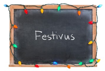 Happy Festivus handwritten in white chalk on a black chalkboard decorated with festive holiday lights isolated on white
