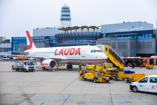 Vienna, Austria - 15 December, 2025: airplane from Lauda is parked at Vienna International Airport. Ground crew is loading luggage onto aircraft. The terminal building is visible in the background.