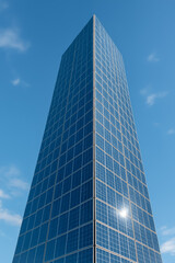 Obraz premium Tall modern glass skyscraper viewed against clear blue sky