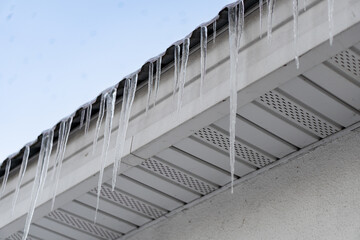 Photo of multiple icicles formed on the roof of house. Big sharp dangerous icicles on the roof right over sidewalk. Winter weather conditions concept. Icicle danger in cities concept.