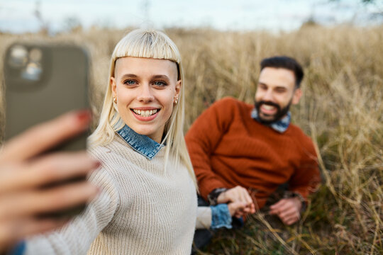 Couple enjoying a relaxing moment together on the grass and taking a selfie with a mobile phone camera  during a sunny day in a field - Powered by Adobe