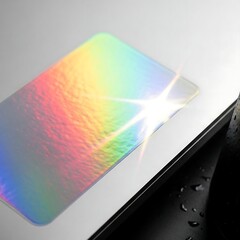 Iridescent Card on White Surface with Rainbow Reflection and Black Edge.