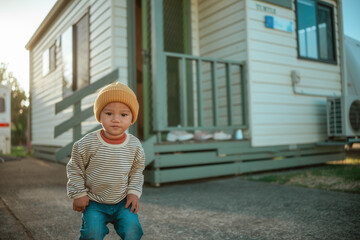 toddler with beanie outside trailer, young child smiling beside retro caravan in evening