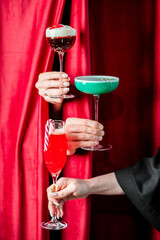 A vertical shot of three different festive cocktails with holiday garnishes being held up in front of a vibrant red curtain, perfect for Christmas celebrations.