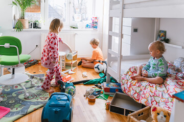 Children's room. Children elementary ages playing and cleaning in messy nursery. Boy vacuums the room while others siblings play. Child's playroom full of toys. Family at home.