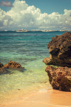 Large coral rocks on the beach, with a cloud-filled sky and boats sailing on the shallow sea in the background at white beach, bor