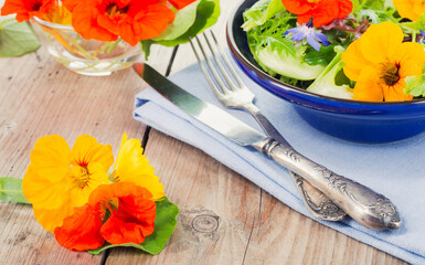 Fresh salad in a bowl topped with edible flowers nasturtium marigold and borage on a rustic wooden table. Colourful healthy food styling for summer menu and wellness.