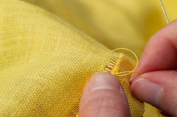 Close up of hand sewing on yellow linen fabric finished with hemstitch. Shallow depth of field highlights needlework detail for handmade crafts DIY hobby and slow living concept