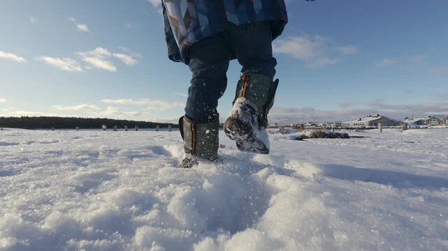 Rear view of a child boy in winter boots and warm clothes walking through snow at sunset. Winter park in Nova Scotia, Canada, golden light, calm atmosphere and seasonal outdoor childhood concept.