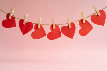 Red paper hearts hanging on a string with clothespins on pink background