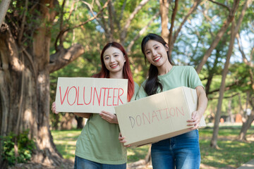 Community Compassion: Two volunteers display signs and boxes, ready to collect donations amidst the peaceful green environment, emphasizing giving and selflessness.