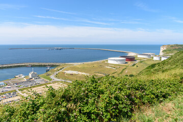 Oil terminal with large steel fuel tanks at the foot of a cliff on a clear summer day