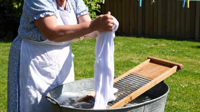 Woman Washing Clothes by Hand Using Wash Tub and Washboard Outdoors on Green Lawn