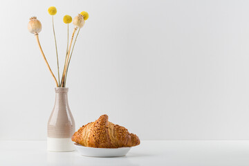 white plate with fresh croissant. A vase with dried flowers
