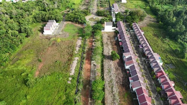 The drone footage shows a long row of townhouses along the main road, surrounded by dense forest and green spaces. 