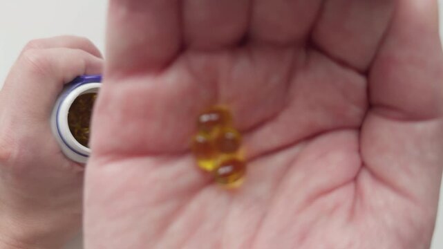 A man pouring vitamin D3 capsules from a plastic bottle into his palm and taking them. Close up.