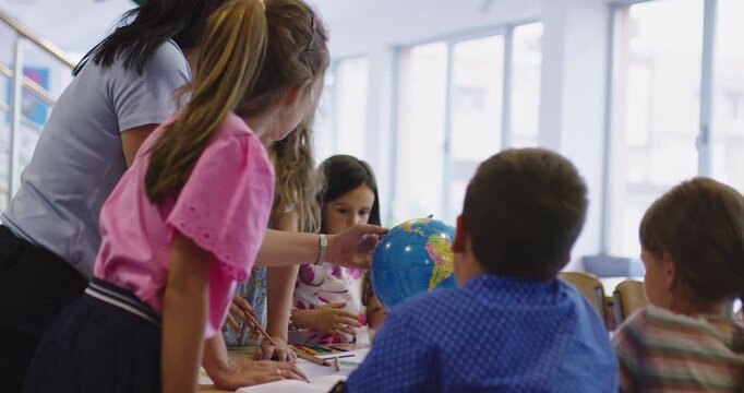 Teacher and elementary students learning geography with globe in classroom, curious children exploring world map together, social studies and global education for kids.