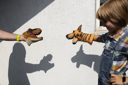 Kids' fun and imaginative shadow play. Two people play with shadows cast on a wall, using dinosaur and dog heads as their hands. Creative ideas for summer fun