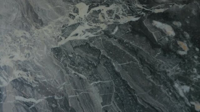 Polished stone surface shows natural veins in gray, white and black. Texture feels smooth and rich. Pattern is calm, elegant and fits well in modern interior design.