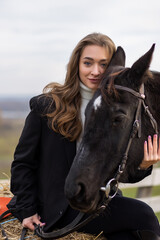 Obraz premium Woman with a black horse outdoors, wearing a coat, sharing a calm, affectionate moment