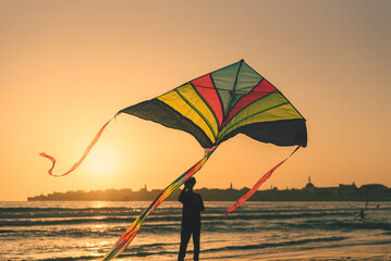Colorful kite flying at sunset beach with silhouette of old city in background - Summer outdoor recreation activity