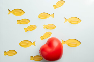 Fish oil soft gel capsules, dietary supplements containing Omega 3 for heart health.  Yellow fish with blue background with a big red heart.  Heart health month February.